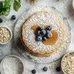 Fluffy buckwheat and oat flour pancakes with honey and fresh blueberries on a white marble table